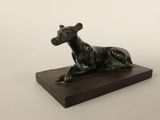 sculpture en bronze représentant un chien, posée sur un socle en bois, sur fond blanc