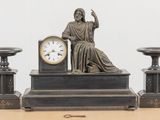 une statue représentant un homme assis sur une table, à côté d'une horloge