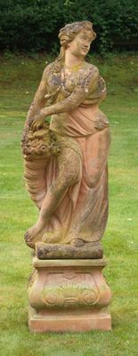 une statue représentant une femme assise sur un socle dans l'herbe