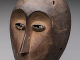 une image représentant un masque en bois posé sur un socle, sur fond gris