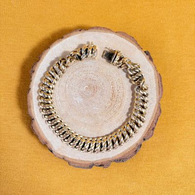 gold chain bracelet on a wood slice on a yellow background