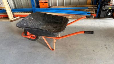 a black wheelbarrow with orange wheels in a warehouse