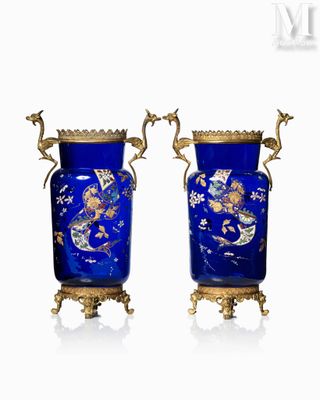 une paire de vases bleus rehaussés de touches dorées, posés sur des socles, sur fond blanc