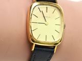 une montre en or avec un bracelet en cuir noir au poignet d'une femme