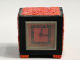 a small black and red clock sitting on a white surface
