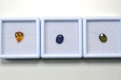 trois pierres précieuses de couleurs différentes se trouvent dans une boîte blanche posée sur une surface blanche