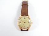 une image représentant une montre en or avec un bracelet marron sur un fond blanc