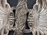 a silver plate with two wings on it on a black surface