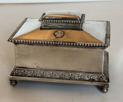 une boîte ancienne en métal argenté avec un couvercle, posée sur une surface blanche