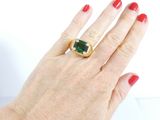 a woman ' s hand holding a ring with a green stone on it