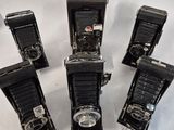 five old cameras are lined up on a white surface
