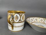two white and gold coffee cups and a bowl on a table