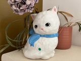 a white cat figurine sitting on a table next to a purple flower