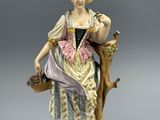 une figurine ancienne représentant une femme assise sur une branche d'arbre, tenant un panier