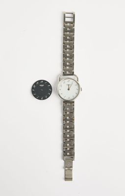 un gros plan d'une montre et d'une pièce de monnaie posées sur une surface blanche