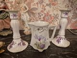 three white vases with purple flowers on them on a table