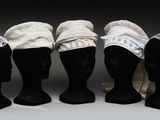 quatre têtes de mannequins coiffées de chapeaux en dentelle, exposées sur un fond gris