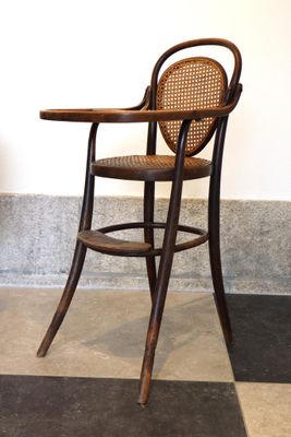 une chaise en bois avec une assise en osier, posée sur un sol à carreaux noirs et blancs