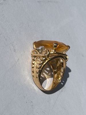 a gold ring with a yellow stone on a white surface