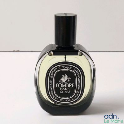 une image représentant un flacon de parfum posé sur une surface blanche