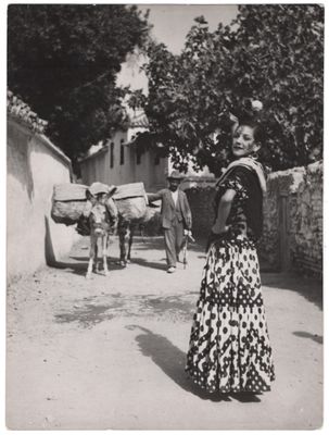 photographie en noir et blanc d'une femme en robe longue, debout dans un village