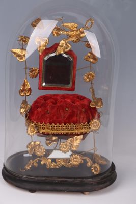 a glass cloche with a red velvet chair under it