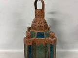 a small copper colored lantern with a green and blue glass inside
