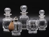six bouteilles en verre transparent munies de bouchons en bois, posées sur un support noir