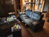 a black leather couch sitting in a living room with books on the floor