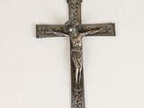 une croix en argent sur un mur blanc, surmontée d'un crucifix