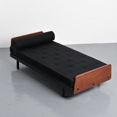 lit de repos en cuir noir avec structure en bois et repose-pieds, posé sur un sol gris