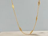 un collier à chaîne en or orné d'une breloque en forme de feuille posé sur une dalle de marbre