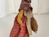 figurine of an old woman carrying a wicker basket on a white surface