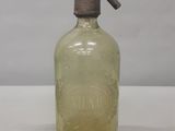 une bouteille en verre à l'ancienne, munie d'un bec verseur en métal, posée sur une surface blanche