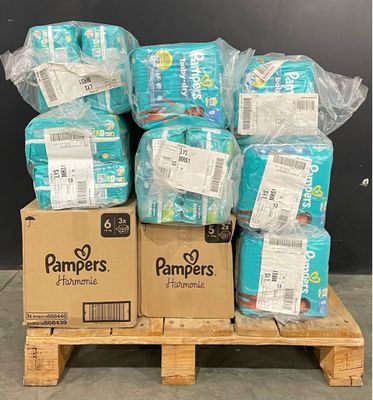 Des cartons de couches sont empilés sur une palette devant un mur noir