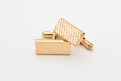 two gold cufflinks on a white surface with a white background