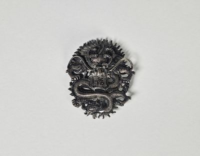 une image représentant une broche en forme de dragon argenté posée sur une surface blanche