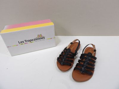 des sandales en cuir noir avec des lanières noires sur un fond blanc, à côté d'une boîte