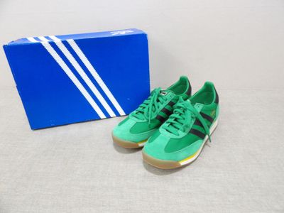 des baskets Adidas vertes et noires posées à côté d'une boîte bleue sur une surface blanche