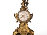 une horloge dorée posée sur un socle, sur une surface blanche