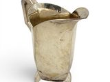 a silver vase with a spoon in it on a white surface