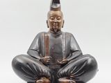 statue d'un homme assis sur un socle en bois, coiffé d'un chapeau