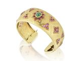 un gros plan d'une bague en or sertie de pierres roses et vertes