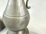 a silver pitcher sitting on top of a table next to a spoon