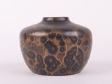 un vase marron parsemé de taches noires sur un fond blanc