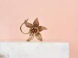 la bague en forme de fleur dorée repose sur un bloc de marbre blanc