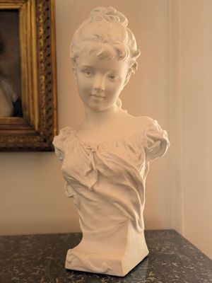 a white busturine on a table in front of a painting