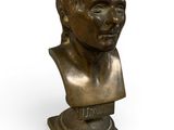 un buste en bronze représentant un homme, posé sur un socle, avec un fond blanc