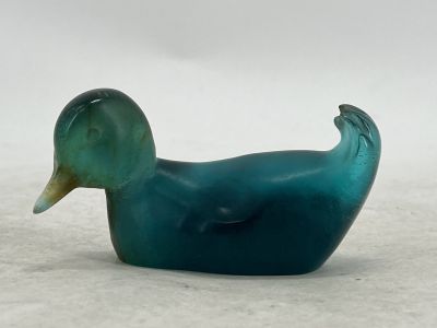 a blue glass duck sitting on a white surface