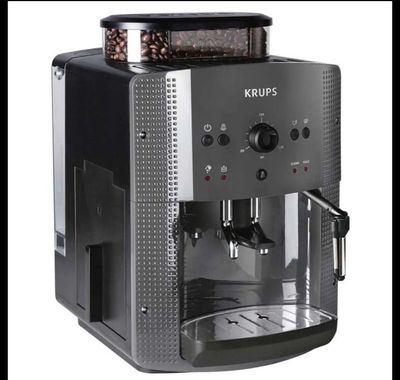 Une machine à café Krups sur fond blanc, avec des grains de café